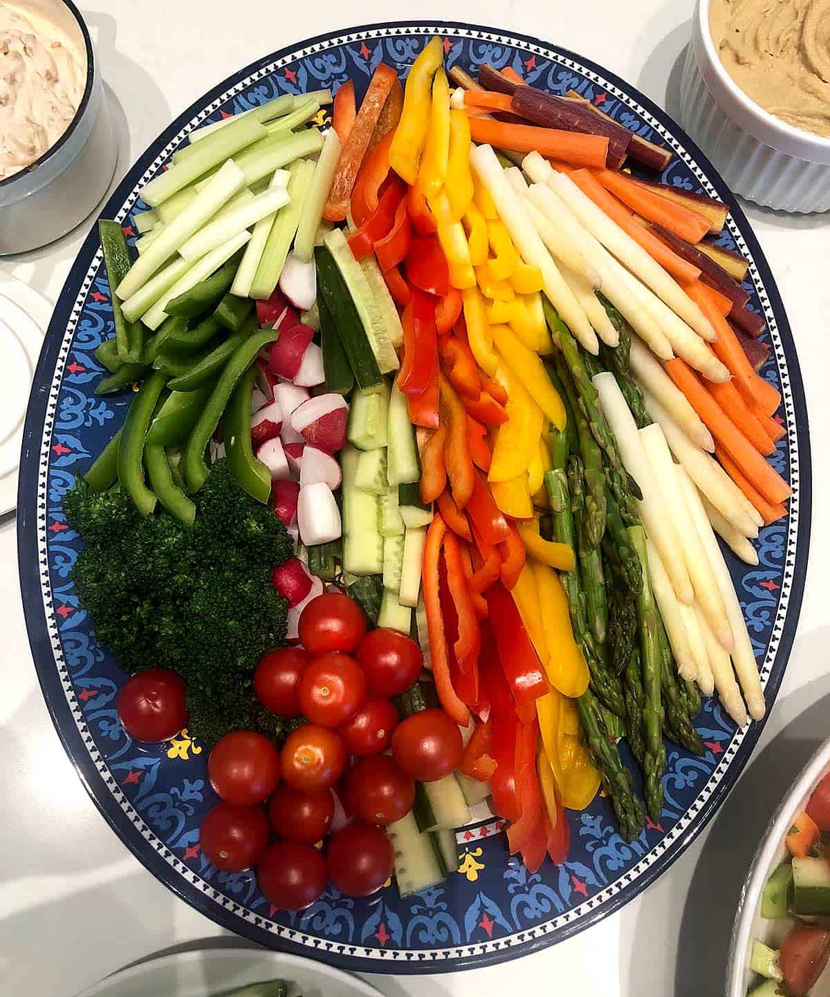 Crudité platter with bell peppers, carrots, zucchini, cucumber, radishes, asparagus, broccoli, and cherry tomatoes with hummus and onion dip