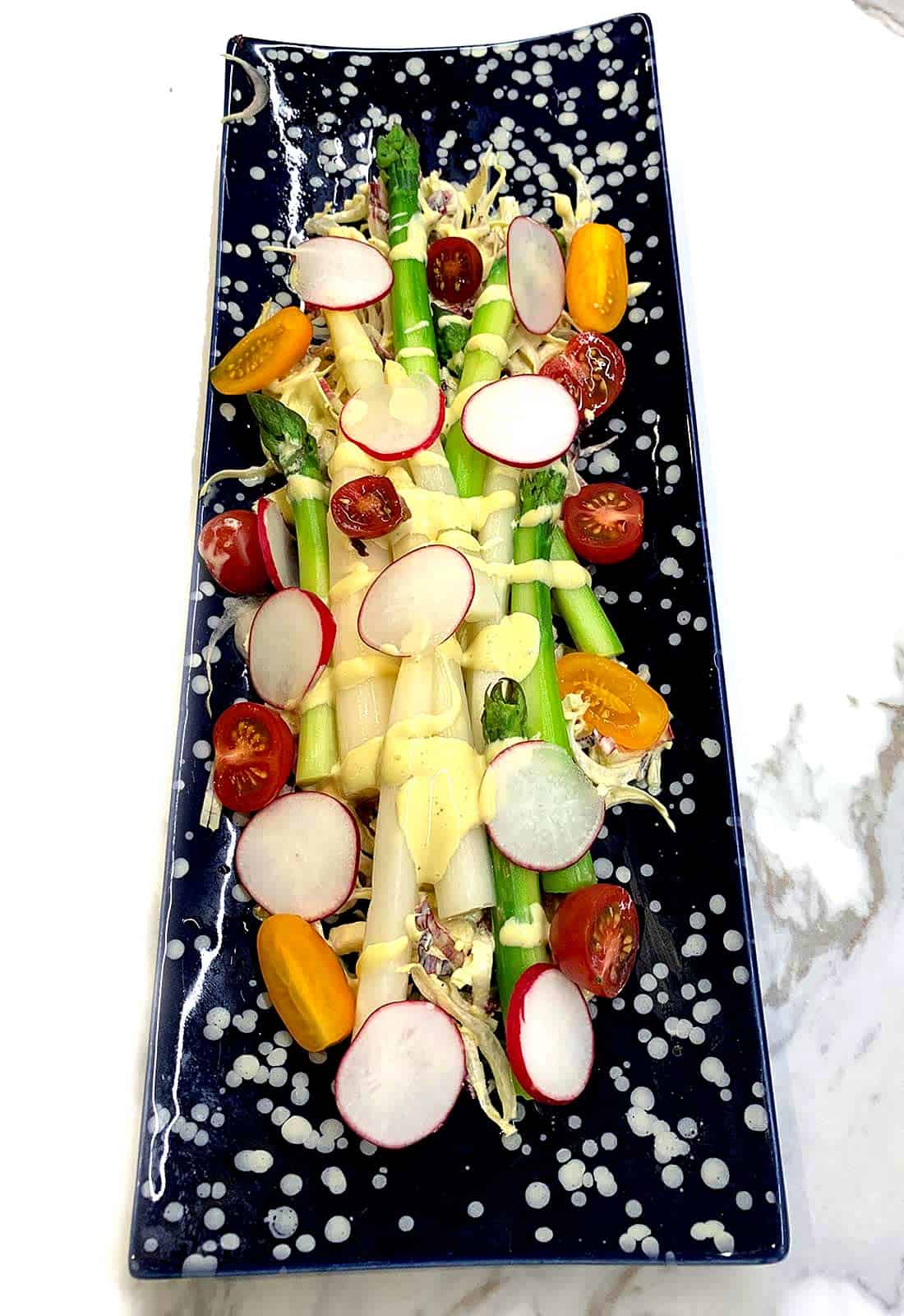 Crudité platter with radishes, cherry tomatoes, and asparagus with cream drizzle