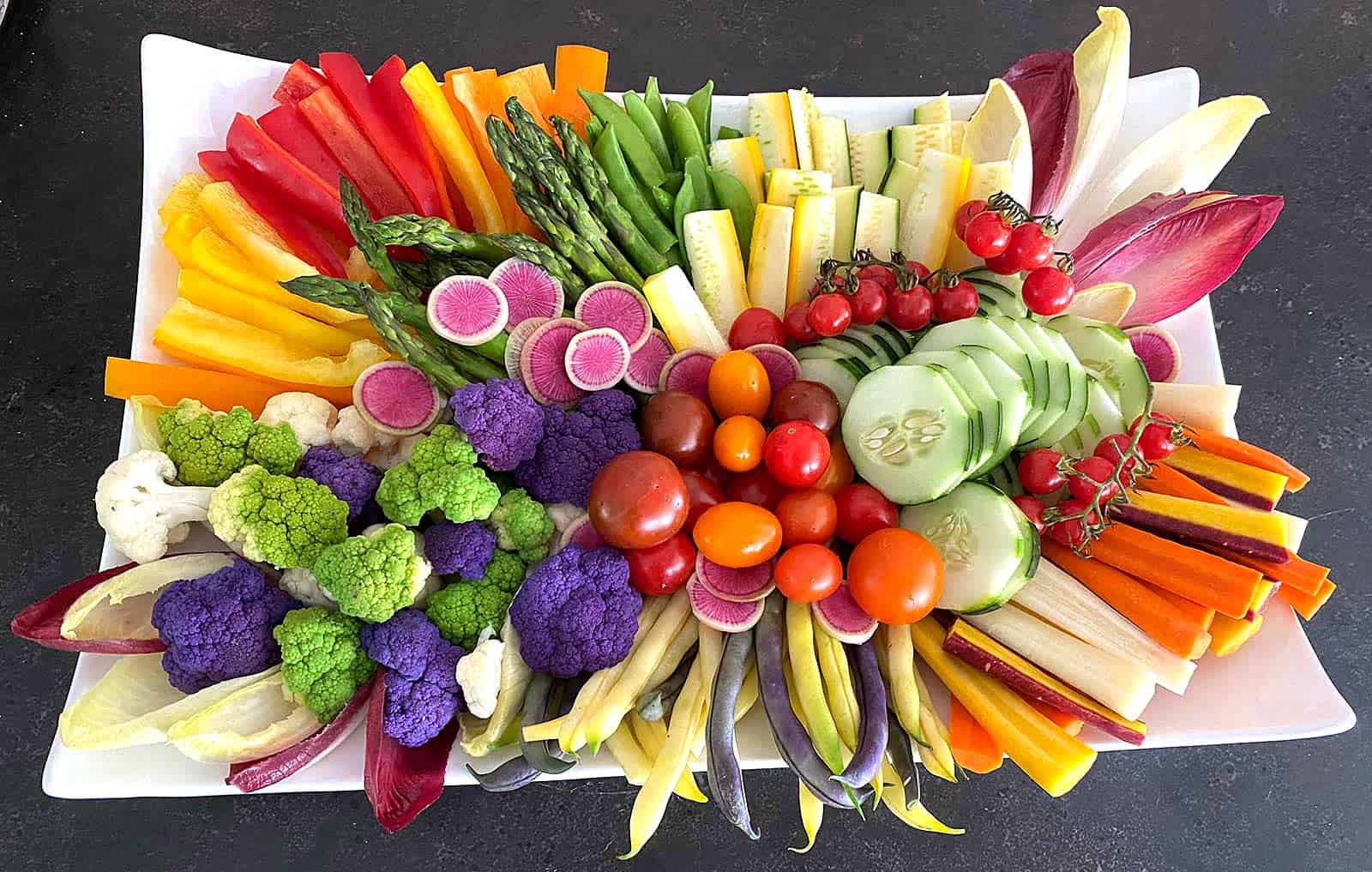 Crudité platter with radishes, cherry tomatoes, asparagus, cucumber, bell peppers, squash, snap peas, green beans, broccoli, carrots, endive, and cauliflower
