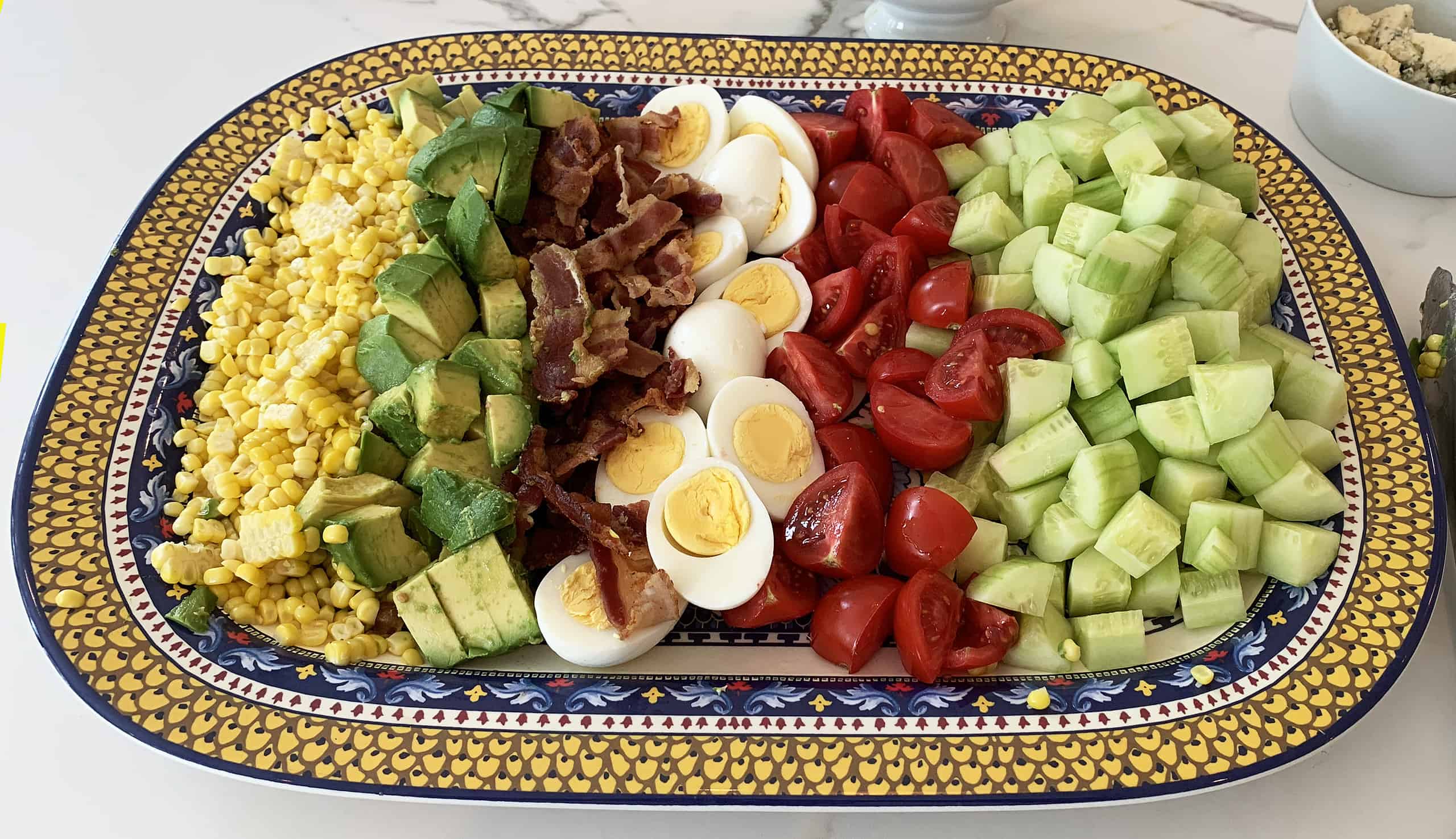 Platter with corn, avocado, bacon, boiled egg, cherry tomatoes, and cucumber